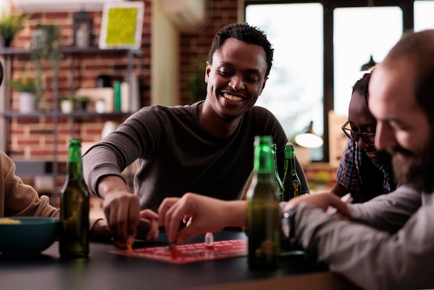 Уверенно улыбающийся афроамериканец играет в настольные игры с друзьями дома.