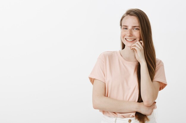 Уверенно улыбающаяся девочка-подросток позирует у белой стены