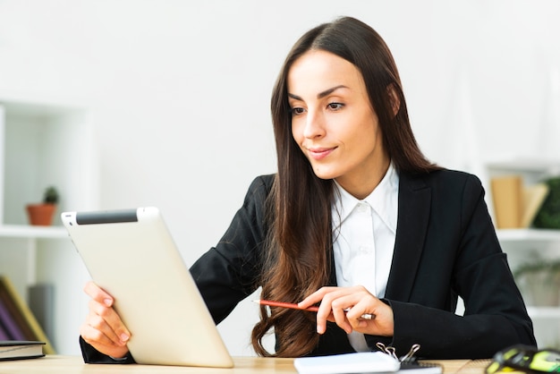 Foto gratuita giovane donna di affari sorridente sicura che esamina compressa digitale nell'ufficio