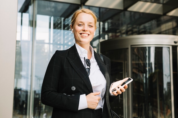 Confident smiling young woman holding mobile phone in hand