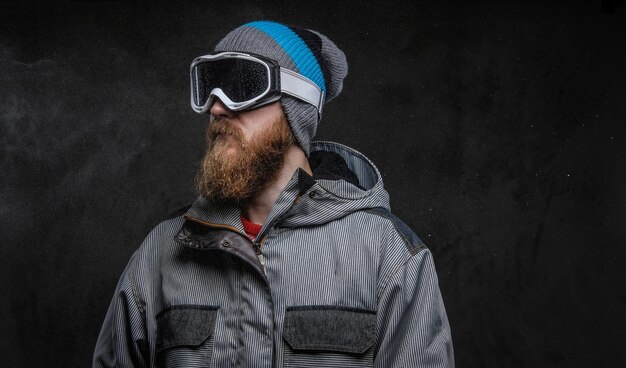 Confident snowboarder wearing full protective equipment, isolated on a dark textured background.