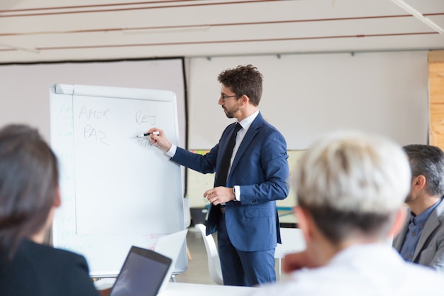 Confident speaker in eyeglasses talking near whiteboard