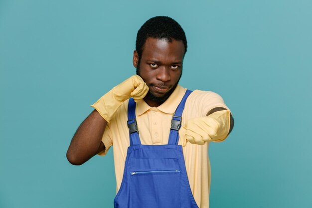 Уверенно стоящий в боевой позе молодой афроамериканец-уборщик в форме с перчатками на синем фоне