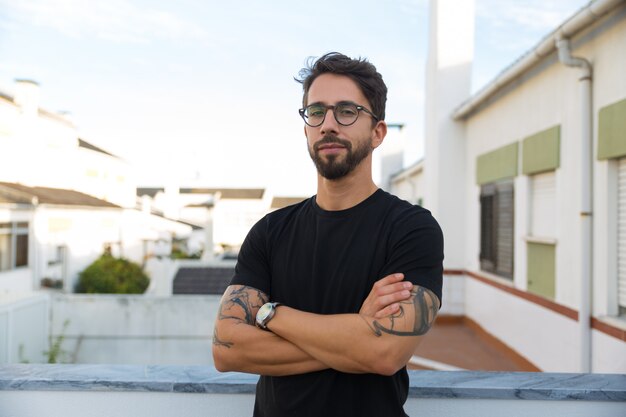 Confident stylish guy with tattoos posing on apartment balcony