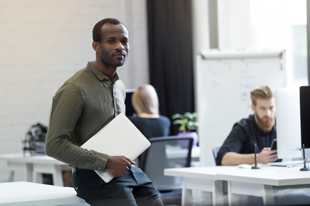 Confident successful african man sitting on a desk with laptop