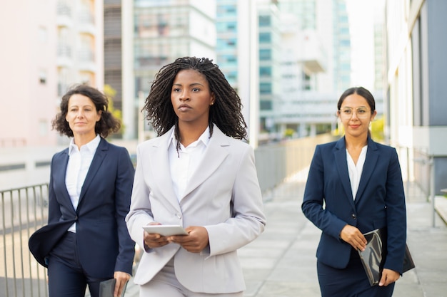 confident team leader holding tablet during stroll. confident businesswomen wearing suits walking on street. teamwork concept
