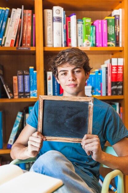 Confident teenager showing chalkboard in library