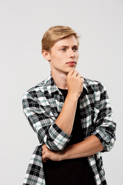 Confident thinking blond handsome young man wearing casual plaid shirt with hands crossed on chest looking away