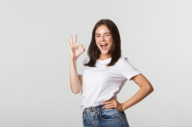 Confident and upbeat attractive girl showing thumb-up gesture in approval.