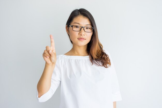 Confident well-educated young woman showing index finger and looking at camera.