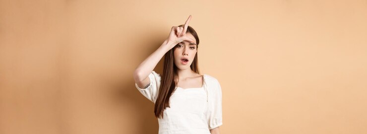 무료 Photo 패자 표시로 사람들을 조롱하는 자신감 있는 여성은 베이지색 배경에 서 있는 것을 의미합니다.