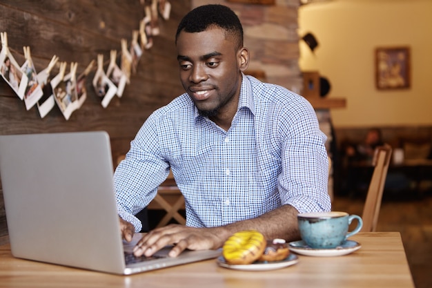 Free photo confident young african-american office worker in formal wear keyboarding on laptop pc