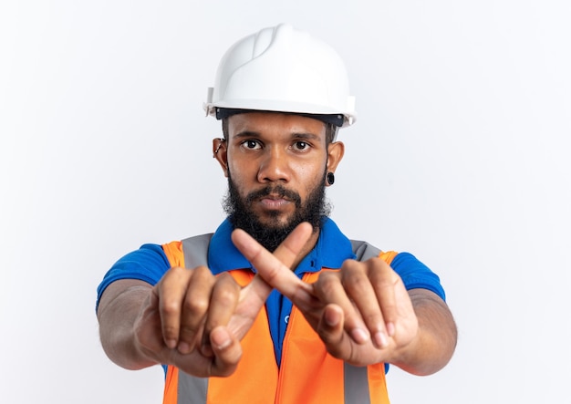 Уверенный молодой афро-американский строитель человек в форме с защитным шлемом, скрестив пальцы, жестикулирующий без знака на белом фоне с копией пространства