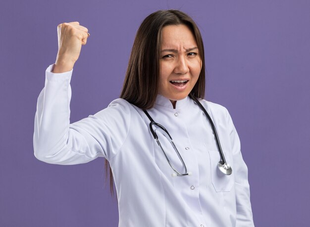 Confident young asian female doctor wearing medical robe and stethoscope doing solidarity gesture  isolated on purple wall