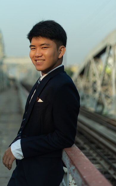 Confident young Asian man in a suit leaning on a bridge