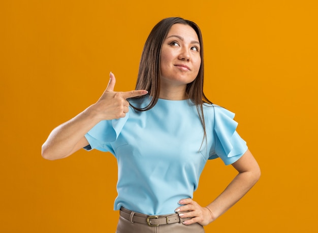 Confident young asian woman looking up pointing side isolated on orange wall