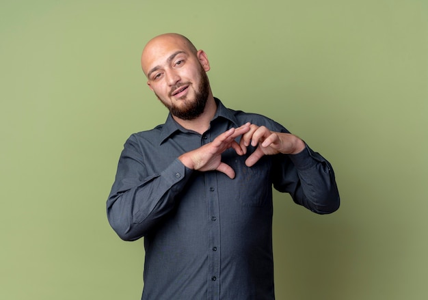 Free photo confident young bald call center man doing heart sign isolated on olive green  with copy space