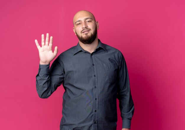 Confident young bald call center man doing hi gesture isolated on crimson  with copy space