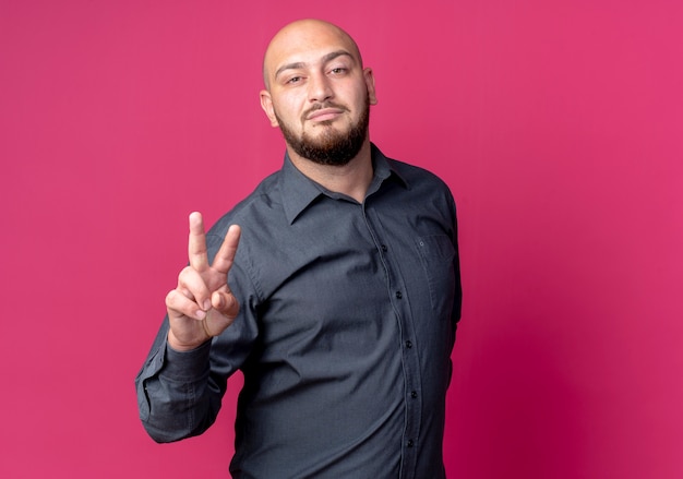 Confident young bald call center man doing peace sign isolated on crimson  with copy space