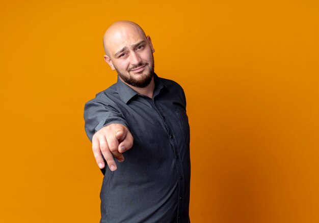 Confident young bald call center man pointing isolated on orange  with copy space