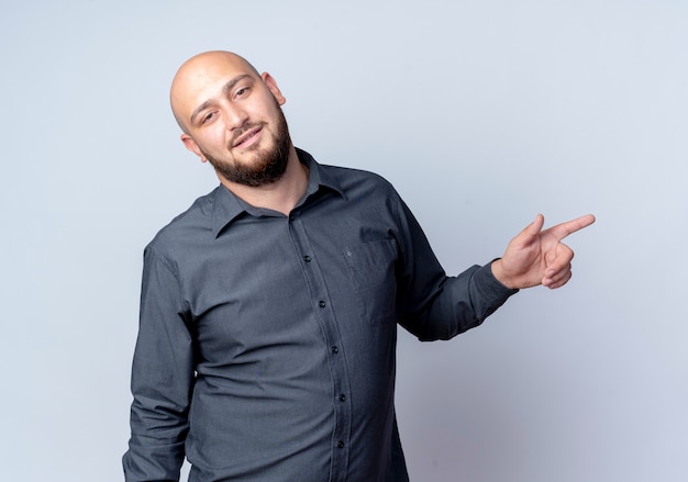 Confident young bald call center man pointing at side isolated on white 