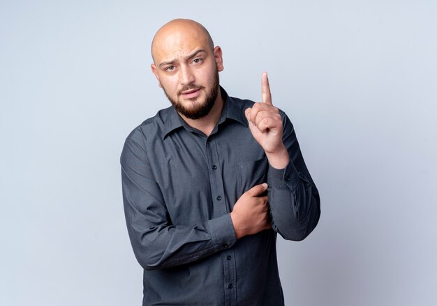 Confident young bald call center man putting hand on chest and raising finger isolated on white  with copy space