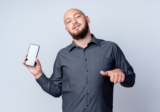 Confident young bald call center man showing mobile phone and pointing at it isolated on white 