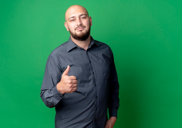 Confident young bald call center man showing thumb up isolated on green  with copy space