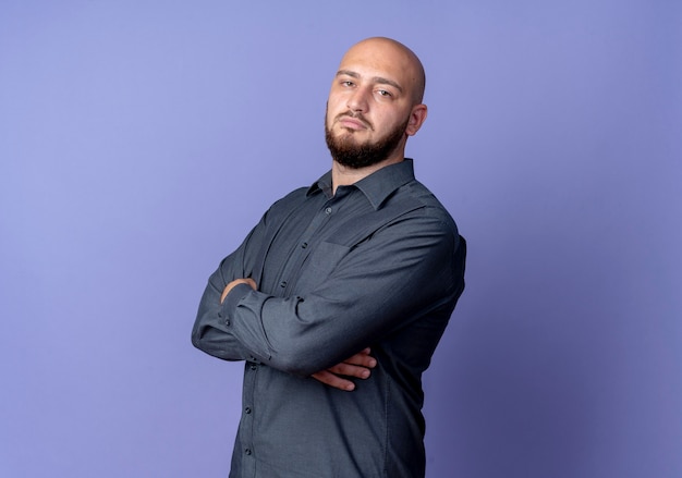 Confident young bald call center man standing with closed posture in profile view isolated on purple  with copy space