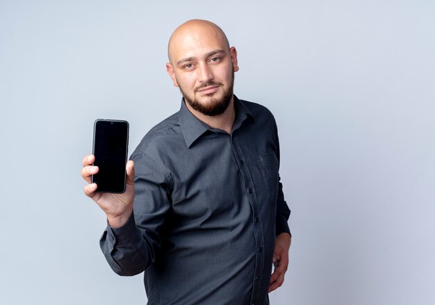 Confident young bald call center man stretching out mobile phone towards camera isolated on white  with copy space