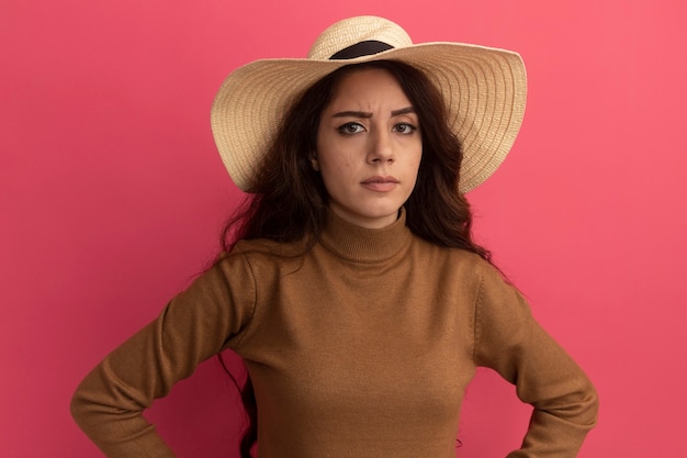 Confident young beautiful girl wearing turtleneck sweater with hat isolated on pink wall