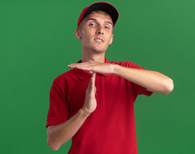 Confident young blonde delivery boy gestures time out hand sign