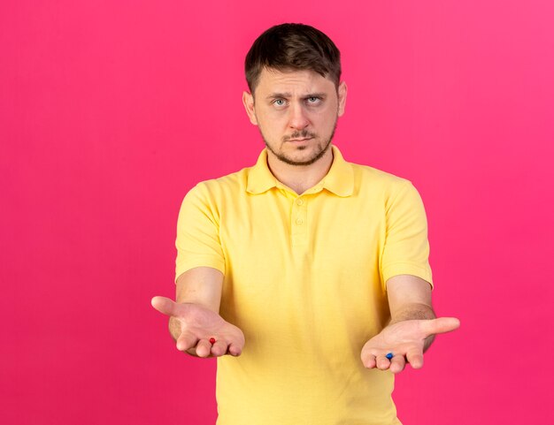 Confident young blonde ill slavic man holds medical capsules in hands on pink