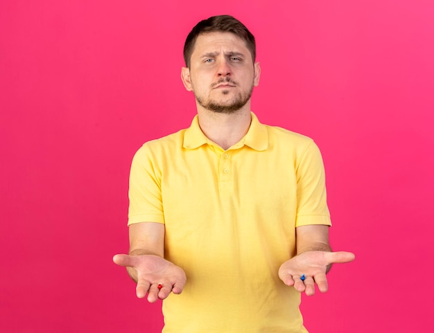 Free photo confident young blonde ill slavic man holds red and blue medical capsules in hands on pink