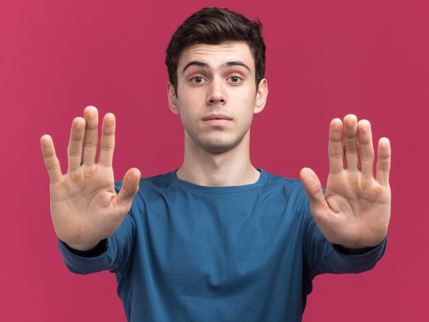 Confident young brunette caucasian boy gesturing stop sign with two hands on pink