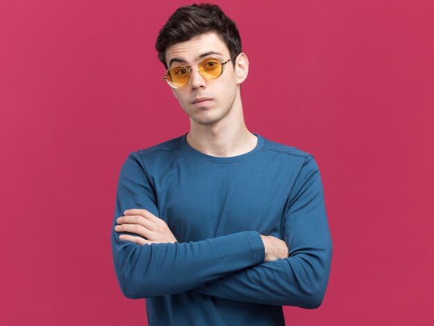 Confident young brunette caucasian boy in sun glasses standing with crossed arms