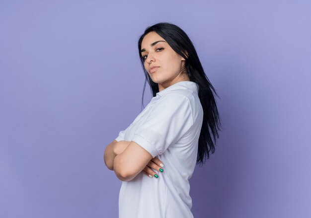 Уверенная молодая брюнетка кавказская девушка стоит боком изолированной на фиолетовой стене