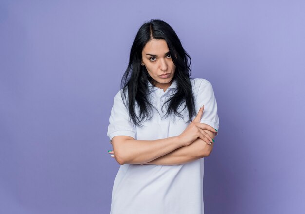 Confident young brunette caucasian girl stands with crossed arms isolated on purple wall