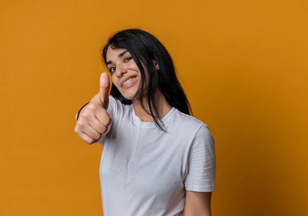 Confident young brunette caucasian girl thumbs up isolated on orange wall