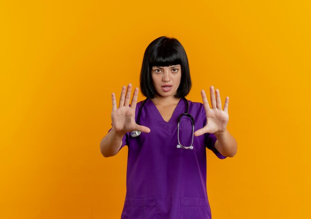 Confident young brunette female doctor in uniform with stethoscope stop hand sign