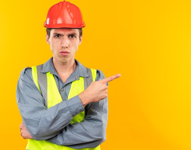 Confident young builder man in uniform points at side 