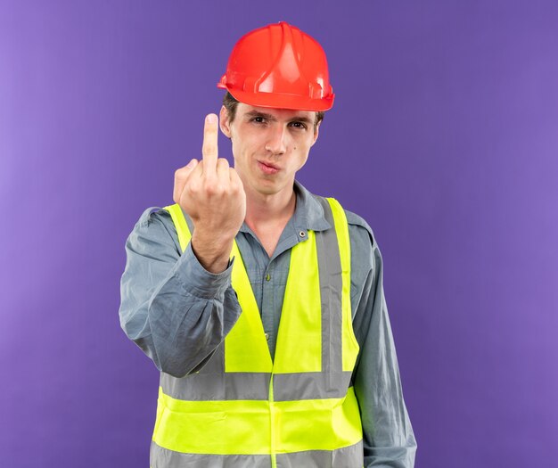 Confident young builder man in uniform showing gesture isolated on blue wall