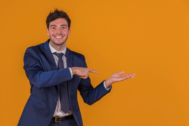 Confident young businessman pointing finger at something against an orange background