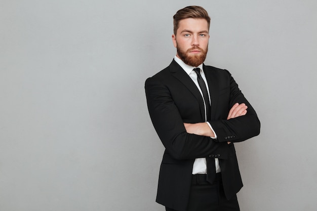 Confident young businessman in suit standing with arms folded