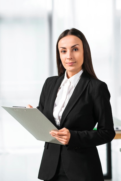 Confident young businesswoman holding clipboard looking at camera