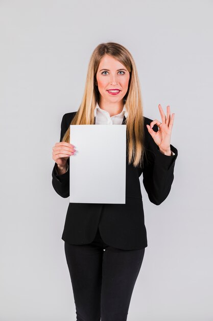 Confident young businesswoman holding the white paper showing ok sign on grey background