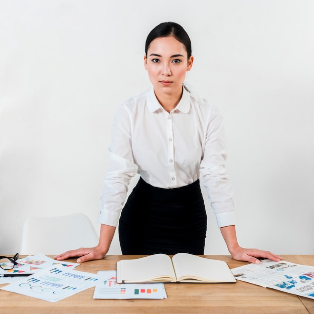 Free photo confident young businesswoman standing at office desk against the white wall