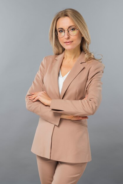 Confident young businesswoman standing with her arm crossed against gray backdrop