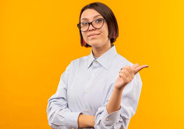 Confident young call center girl wearing glasses pointing at side isolated on orange  with copy space