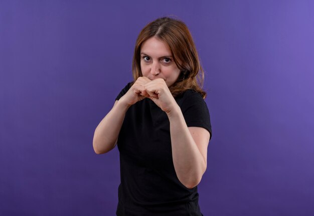 Confident young casual woman doing boxing gesture on isolated purple space with copy space